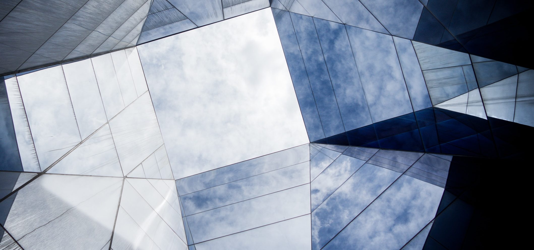 Architectural photo of angular glass planes against a cloudy blue sky