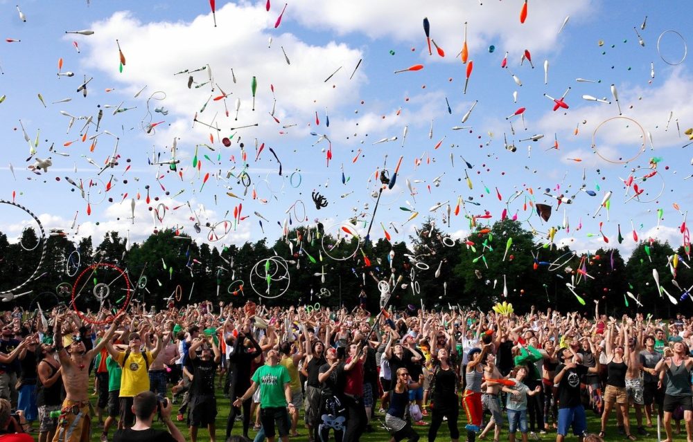 Photograph of a sea of people juggling, with very little of a field visible between legs and a blue sky filled with all kinds of objects